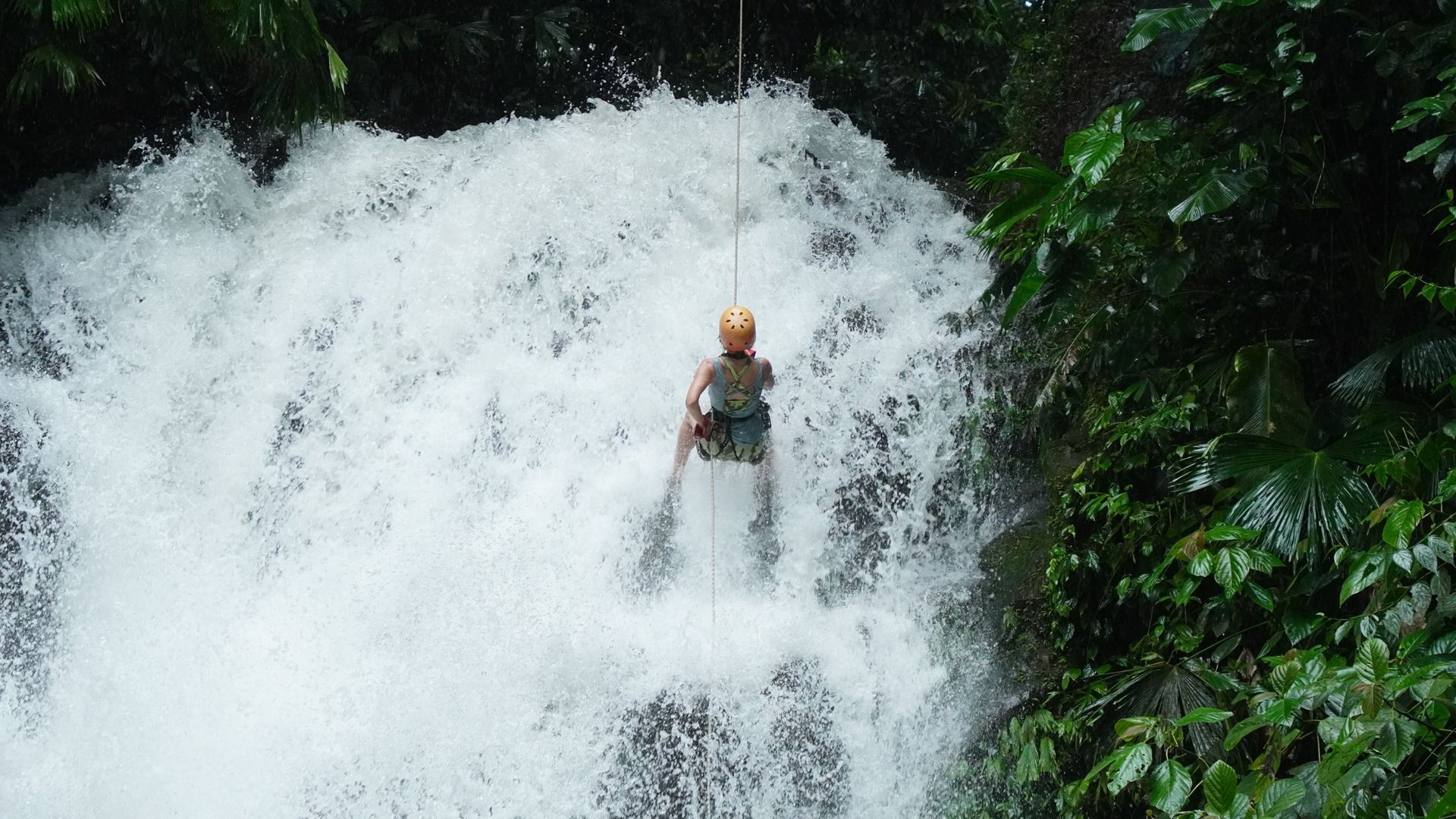 Adventurous canyoning rappelling descent in a scenic canyon with rugged rock formations and flowing waterfall